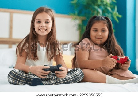 Two kids playing video game sitting on bed at bedroom