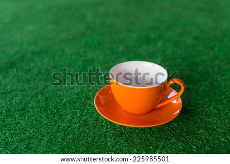 Blank Orange coffee cup on green grass, selective focus. 