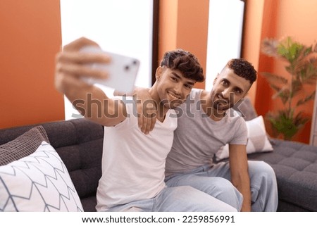 Two hispanic men couple make selfie by smartphone sitting on sofa at home