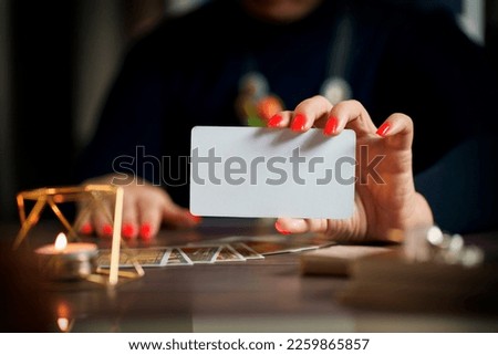 Blank card in female and and blurred tarot cards on table near burning candles in candle light. Forecasting concept. Selective focus                                