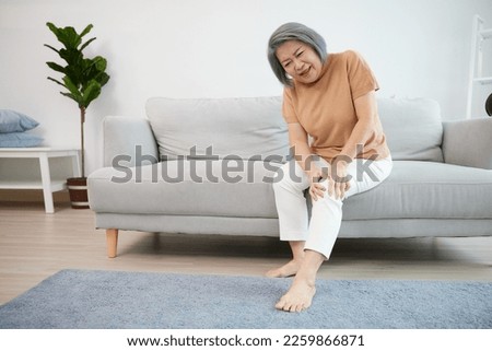 senior woman suffering from knee ache on sofa Royalty-Free Stock Photo #2259866871