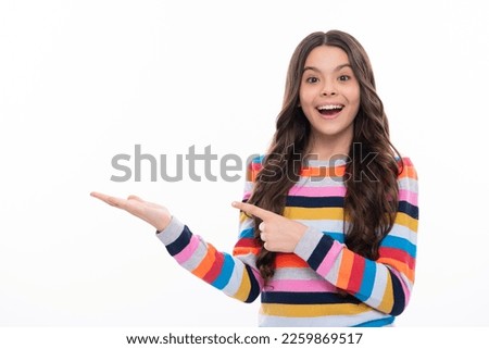 Positive teenager child points aside with cheerful expression, shows amazing at blank empty space. Advertisement and mockup. Excited face, cheerful emotions of teenager girl.