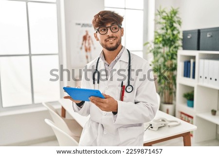 Young arab man wearing doctor uniform using touchpad working at clinic
