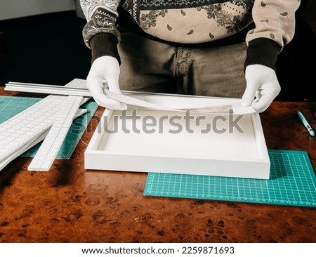A photographer in white gloves frames his photo in a white frame. Hand shot with no face.