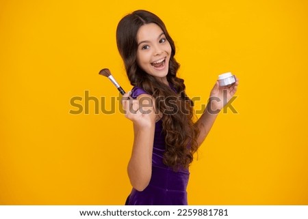 Teenage girl making beauty make up, hold powder and brush. Beautiful teen applying makeup using powder brush isolated on yellow background. Happy girl face, positive and smiling emotions.