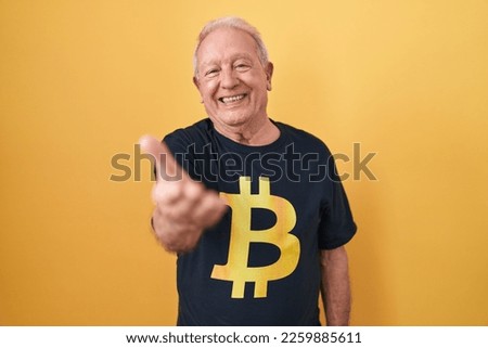 Senior man with grey hair wearing bitcoin t shirt smiling cheerful offering palm hand giving assistance and acceptance. 