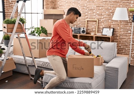 Young hispanic man unpacking cardboard box at new home