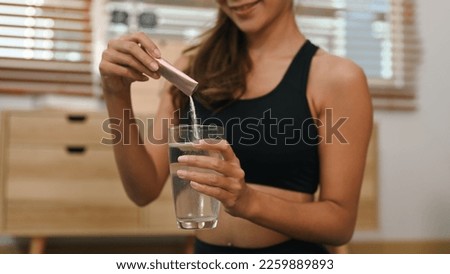 Young woman dissolving collagen powder in glass of water, preparing healthy supplement after exercise Royalty-Free Stock Photo #2259889893