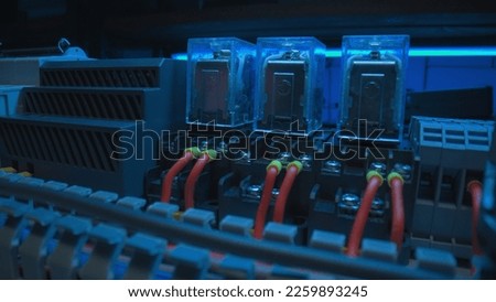 Relay with electromagnetic coils of direct and alternating current, red wires with yellow bushing ferrules. Automatic electrical switch in an electrical workshop. Close up of electrical parts. Royalty-Free Stock Photo #2259893245