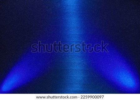 On a dark finely grained background, the central light blue and side blue rays of light