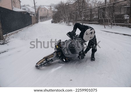 A motorcyclist trying to lift the motorcycle up on a snowy road, a fall, an incident due to a slippery surface. It is impossible to move under such conditions. Motobiker and motorcycle.