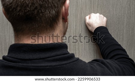 A young man in a black jacket knocks on the door. A visit to someone's home. Knocking by hand