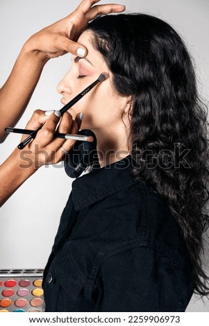Stock photo of young make up artist doing makeup to pretty model in studio.