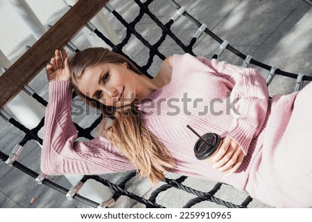 blonde in a hammock with cup of coffee on vacation in the park