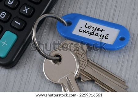 Bunch of keys with a key fob with unpaid rent written in french on it lying near a calculator