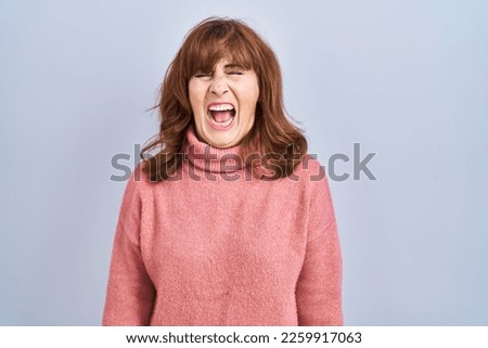Middle age hispanic woman standing over isolated background angry and mad screaming frustrated and furious, shouting with anger. rage and aggressive concept. 