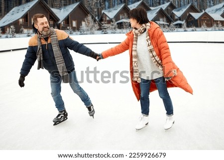 Mature, middle-aged man and woman, couple skating on open air ice skate in winter day. Outdoor weekends. Concept of leisure activity, winter hobby and sport, vacation, fun, relationship, emotions.