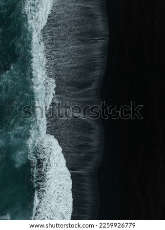 A vertical aerial top view of dark sea waves coming onto the shore