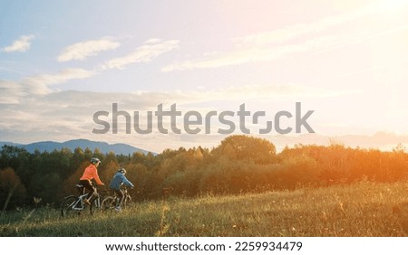Mother and son ride a bike. Happy cute boy in helmet learn to riding a bike in park on green meadow in autumn day at sunset time. Family weekend.  Royalty-Free Stock Photo #2259934479