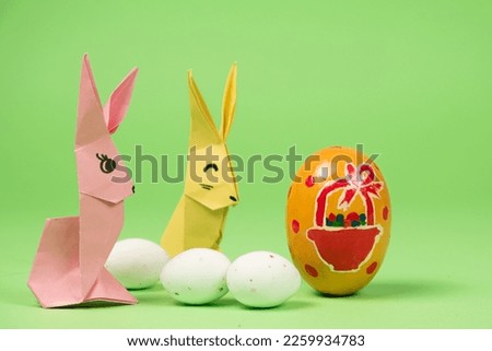 Easter origami - two paper bunnies and eggs, green background. Crafts for the holiday, do it yourself