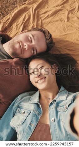 Close up, happy couple taking selfie while lying on blanket in the park. Top view