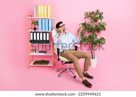 Full size photo of young confident successful office manager guy sit comfort chair talking phone near furniture isolated on pink color background