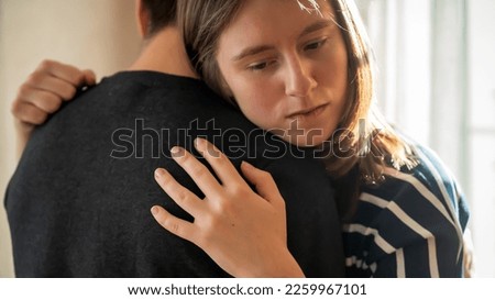 Happy young girl warmly hugs her boyfriend, rejoices at the meeting, stands near the window, smiley face in close-up, woman starts a romantic relationship. Husband and wife feel united, in a harmony.