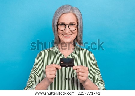 Photo of cheerful aged lady toothy smile arms hold plastic debit card isolated on blue color background