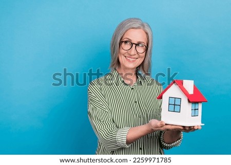 Photo of dreamy sweet mature woman realtor wear shirt spectacles holding house looking empty space isolated blue color background