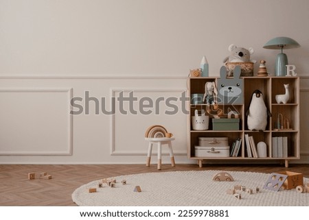 Interior design of kid room interior with copy space, wooden sideboard, round rug, beige wall with stucco, plush toys, white stool, wooden blockers and personal accessories. Home decor. Template. 