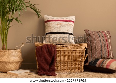 Minimalist composition of living room with colorful pillows, stylish wicker basket, claret plaid, beige wall, plants in basket, book, brown wall and personal accessories. Home decor. Template.  Royalty-Free Stock Photo #2259978965