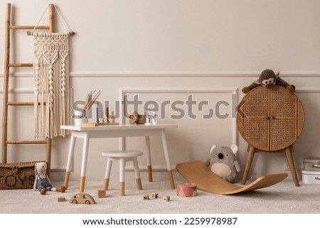 Warm and cozy kids room interior with white desk, stool, rattan sideboard, stylish toys, plush monkey, koala, macrame, wooden blockers, beige rug and personal accessories. Home decor. Template. 