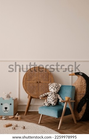 Minimalist composition of kid room interior with blue armchair, plush toys, wooden blocks, rattan sideboard, beige wall with stucco, braided penguin and personal accessories. Home decor. Template.