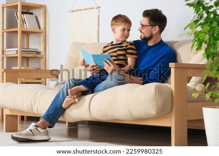Father reading book with his son on sofa in living room at home