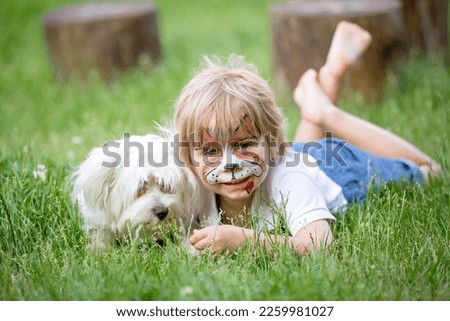 Little toddler baby boy, child with painted face as a dog, playing with pet dog in the garden on birthday party