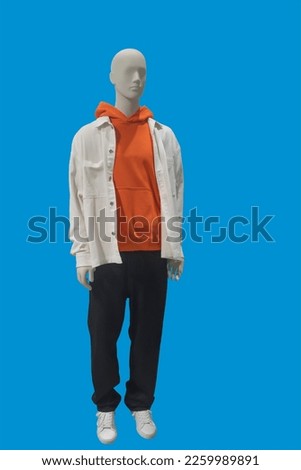 Full length image of a male display mannequin dressed in white jacket, red sweatshirt with hood and black jeans isolated on blue background.  Royalty-Free Stock Photo #2259989891