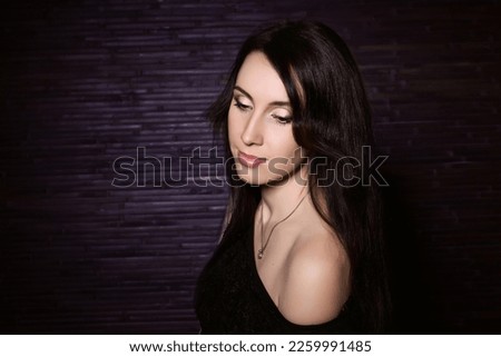 Portrait of a beautiful brunette with long hair and a bare shoulder on a dark background. Horizontal. Place for text