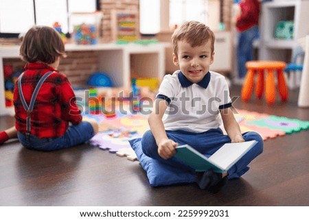 Two kids reading book sitting on floor at kindergarten