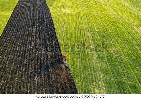 landscape on a farmers field view from a drone, a tractor plows the land. diagonal lines of plants on the ground