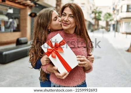 Mother and daughter hugging each other and kissing holding birthday gift at street