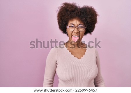 Young african american woman standing over pink background sticking tongue out happy with funny expression. emotion concept. 