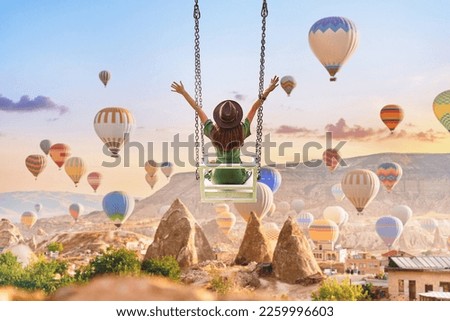 Dreaming woman swinging in Kapadokya. Flying hot air balloons in Anatolia. Happy moment life in beautiful destination in Goreme, Nevsehir  Royalty-Free Stock Photo #2259996603