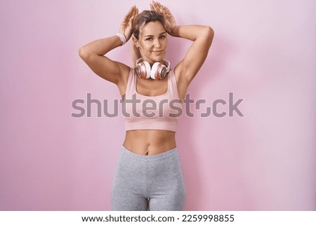 Young blonde woman wearing sportswear and headphones doing bunny ears gesture with hands palms looking cynical and skeptical. easter rabbit concept. 