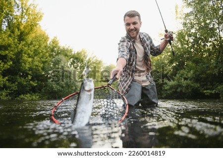 Man with fishing rod, fisherman men in river water outdoor. Catching trout fish in net. Summer fishing hobby. Royalty-Free Stock Photo #2260014819