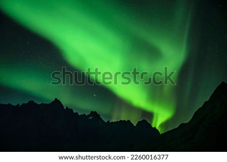 A scenic view of Northern Lights over silhouettes of maountains