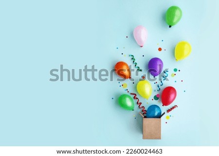 Birthday party flat lay with colorful balloons and confetti escaping from a gift box