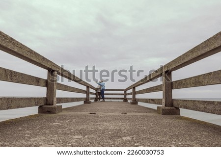 two girls are standing in jackets on a bridge in the distance and taking pictures on the phone, there is a place for an inscription beautiful sea landscape