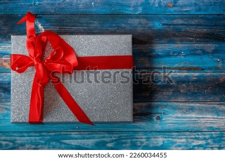 A top view of a gray sparkly Christma present with a red ribbon