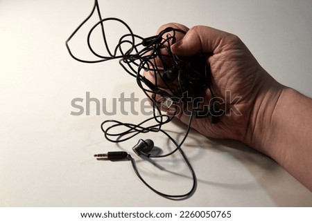 A man's hand with tangled wires from headphones in a hand clenched into a fist close-up, white background
