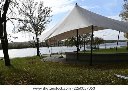 there is a stage with a tented roof in the park by the river